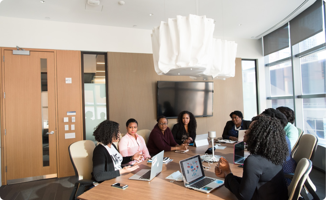 A group of women sitting at a conference table with their laptops having a meeting about Spanish speaking markets.